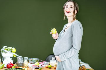 Beautiful pregnant woman with variuos of healthy food on the green background. Healthy eating and wellness during the pregnancy concept