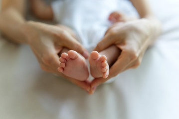 Baby girl feet in her mother hand. Tiny Newborn Baby's feet on female heart Shaped hands seen in top view. Beautiful conceptual image of Maternity. Mom and baby, happy Family concept.