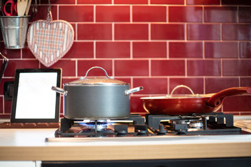 Pot cooking on gas and tablet with recipe.