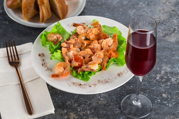 salad with Royal prawns on a white plate on the dark surface of the table with Cutlery.