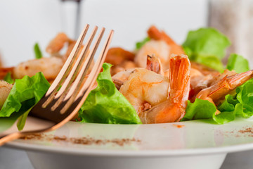 salad with Royal prawns on a white plate on the dark surface of the table with Cutlery.