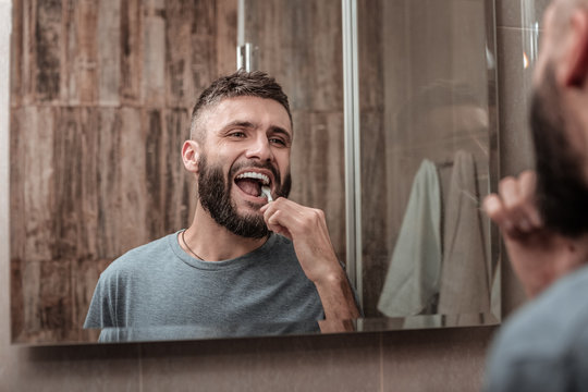 Cheerful dark-eyed mature man brushing his teeth in the morning
