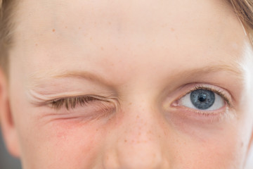 Obraz premium close up of an 8 year old's blue eyes with one eye closed winking