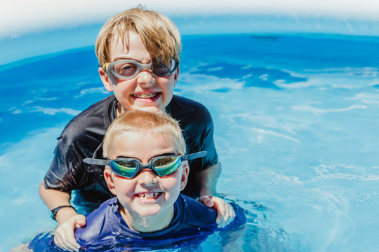 Two boys (brothers) in a pool swimming with goggles on and smiling