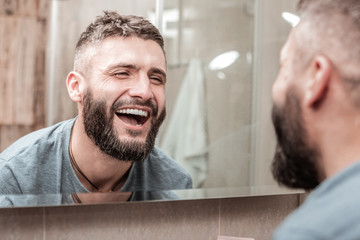 Happy joyful man looking at his face in the mirror