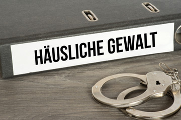 Handschellen und ein Ordner mit dem Aufdruck Häusliche Gewalt