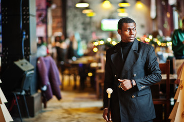Stylish african american gentleman in elegant black jacket, holding retro walking stick as cane flask or tippling cane with golden diamond ball handle. Rich fashionable afro man.