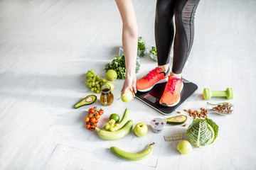 Sports woman weighing on the scales with healthy food around. Weight loss, healthy food and sports lifestyle concept