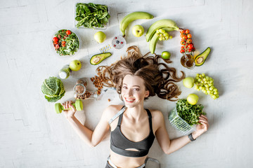 Beauty portrait of a sports woman surrounded by various healthy food lying on the floor. Healthy...