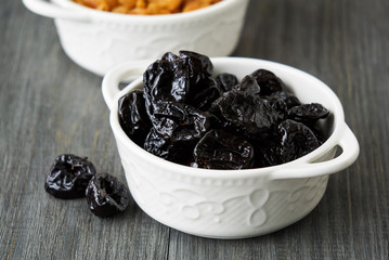 Prunes in a white bowl on a wooden background    