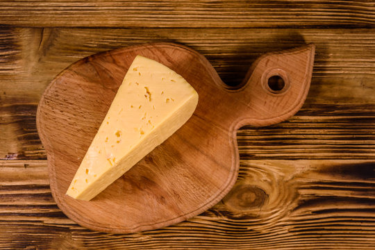 Cutting board with piece of cheese on wooden table. Top view