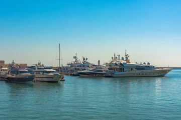 Fototapeta na wymiar Sea port in summer. Many different yachts and boats stand at the marina. Yachtsmen and travelers are preparing to sail in the sea. In the background of the building of the seaside city.