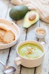 bowl of broccoli and green peas cream soup in a white bowl with avocado