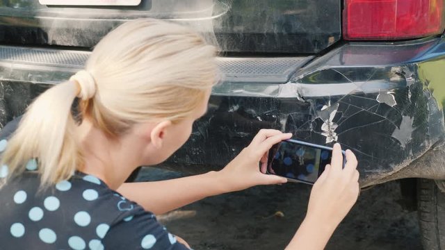 A woman photographs a damaged car bumper