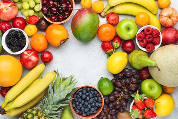 Rainbow fruits background frame, strawberries raspberries oranges plums apples kiwis grapes blueberries mango persimmon on white table, top view, copy space for text, selective focus