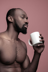 African man with white cup of tea, isolated on pink studio background. Close up portrait in minimalism style of a young naked happy afro man - obrazy, fototapety, plakaty