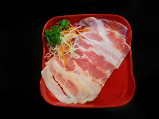 Top view of raw bacon with carot and cabbage in red dish isolated on black background in restaurant at Thailand, fresh meat for grill, Shabu is korea traditional or Sukiyaki is japanese traditional