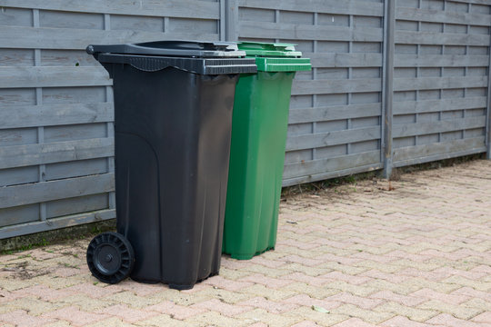 Green black grey recycle bins align a neighborhood street