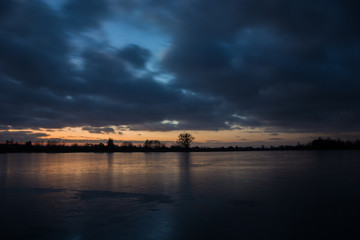 Cloudy dark sky after sunset on a frozen lake and reflecting light on the ice