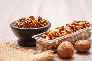 Walnuts in stone bowl and plastic container on a wooden background.