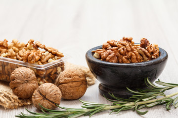 Walnuts in stone bowl and plastic container on a wooden background.