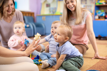 Nursery teacher and babies playing with educational toys in kindergarten or day care centre - obrazy, fototapety, plakaty