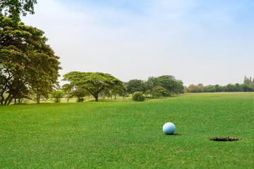 Beautiful landscape of golf course with white golf ball on green grass near hole on background. Golf ball on the green