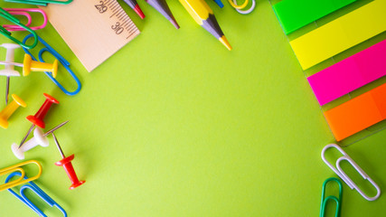 Stationery on green background. Pens, pencils, scissors, paper clips, color push pins and on the table. View from above with copy space