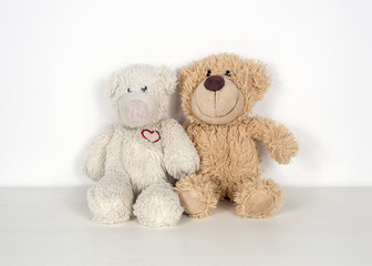 Two teddy bears sit side by side and embrace each other.