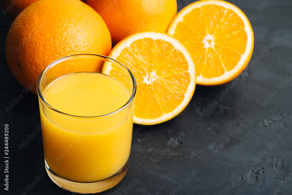 Wall mural orange fresh drink, glass of juice and ripe citrus fruits on a black, textured background