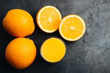 Orange fresh drink, glass of juice and ripe citrus fruits on a black, textured background, top view