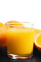 Orange fresh drink, glass of juice and ripe citrus fruits on a black, table and white background