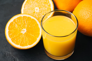 Orange fresh drink, glass of juice and ripe citrus fruits on a black, textured background