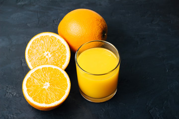 Orange fresh drink, glass of juice and ripe citrus fruits on a black, textured background