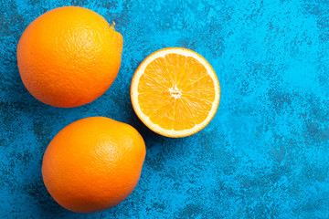 Orange halves and whole ripe citrus fruits on a blue background, top view