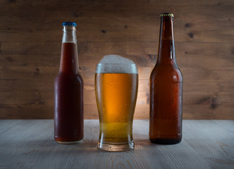 Beer in glass and bottles on wooden background.