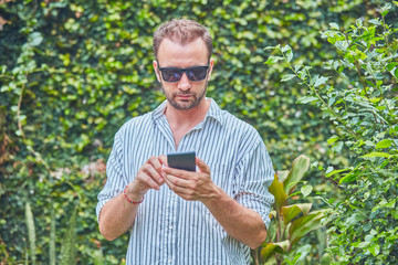 Man with sunglasses and summer shirt using smartphone.