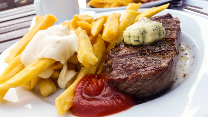 Rindfleisch Steak mit Pommes, Mayo, Ketchup und Kräuterbutter draußen im Biergarden auf Holztisch