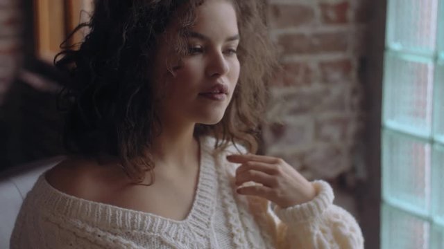 Close up video portrait of young beutiful cute curly girl posing near the window. Natural day light