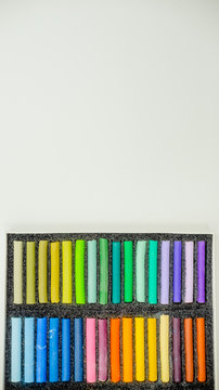 Close up view of bright colorful pastel chalks  on white background. Set of multicolored pastel crayons in openartist box on a white background, top view.