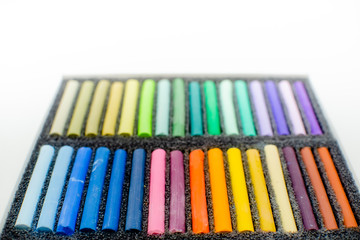 Close up view of bright colorful pastel chalks  on white background. Set of multicolored pastel crayons in openartist box on a white background, top view.
