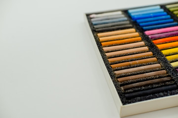 Close up view of bright colorful pastel chalks  on white background. Set of multicolored pastel crayons in openartist box on a white background, top view.