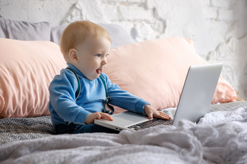 A little boy sits on a big bed and looks curiously at the laptop book
