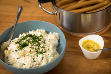 Norddeutscher Kartoffelsalat mit Mayo, Ei und Gurke in Schale, Wiener Würstchen in Kochtopf und Senf auf Holz Tisch