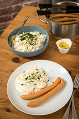 Wiener Würstchen im Topf, Senf und  Norddeutscher Kartoffelsalat mit Mayonnaise, Ei und Gurke als Mahlzeit auf Holz Tisch
