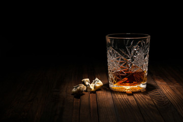 Crystal glass of whiskey on a wooden table on a black background. Snack for whiskey. Cheese, almonds, pear, apple, olives, orange peel.