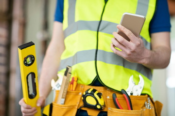 Detail Of Construction Worker On Building Site Wearing Tool Belt Using Mobile Phone