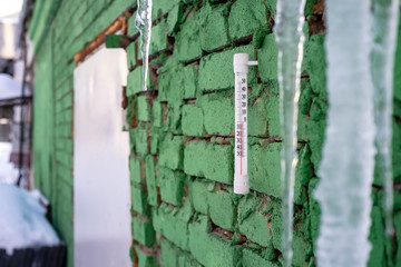 mercury thermometer hanging on a green brick wall, icicles hanging from the roof during a thaw
