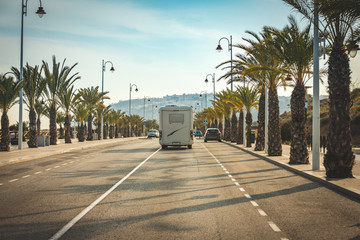 Motorhome arriving in summer paradise in street full of coconut palms and palm trees in beach town....