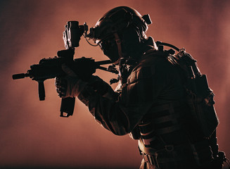 Army soldier, counter terrorist squad fighter, military company mercenary in ammunition and body armor, helmet with night vision device, aiming with short barrel service rifle, low key, studio shoot